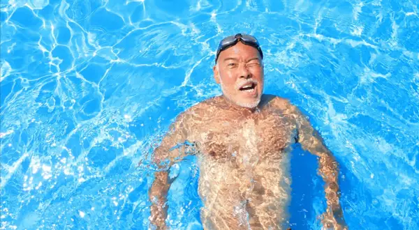 Man in pool, goggles on, with a surprised expression, experiencing immersion diuresis.