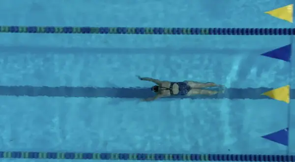 A swimmer glides through the water, executing a powerful breaststroke. The blue pool is marked with lane lines and colorful flags.