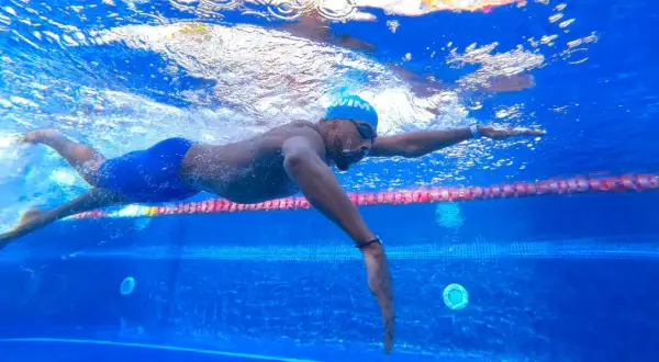 Swimmer in blue cap and goggles glides through the water, a powerful stroke that can help you increase your VO2 max.