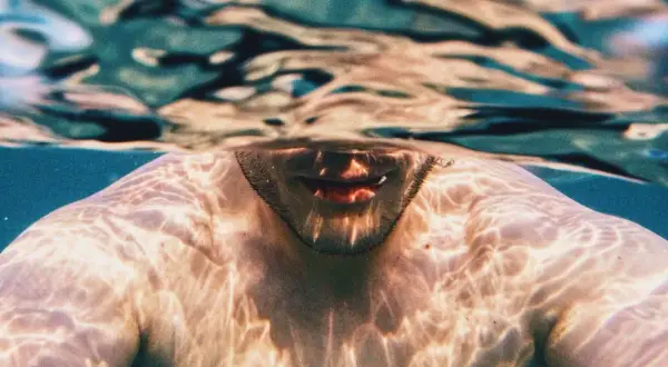 Underwater shot of a man's shoulders and mouth, with light patterns on his skin. A visual guide on how to breathe underwater for beginners.