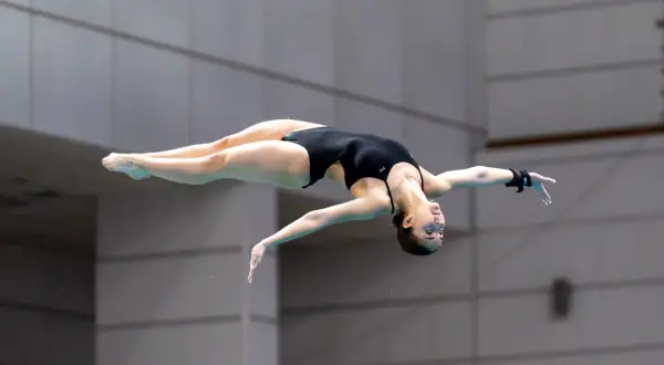 A diver executes a perfect pike position mid-air, body bent at the hips with legs straight and together.