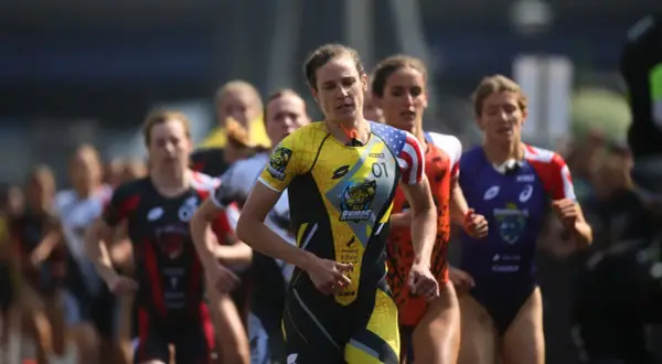 Katie Zaferes, number 01, leads a pack of triathletes in a race, her yellow and black suit featuring a rhino logo.