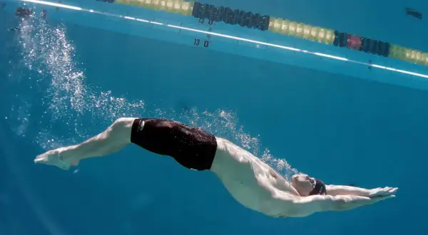 Underwater view of a swimmer performing a powerful kick, showcasing effective leg workouts for swimmers. Bubbles trail behind as they glide through the blue water.