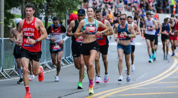 Runners in a marathon, some wearing "Greater Boston" gear, push through the race. The image captures the intensity of the iron man marathon length.