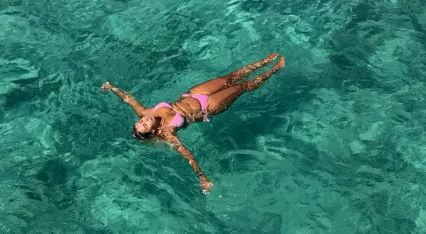 A woman in a pink bikini floats on her back in clear turquoise water. She's enjoying the water, and yes, you can swim with a tampon.