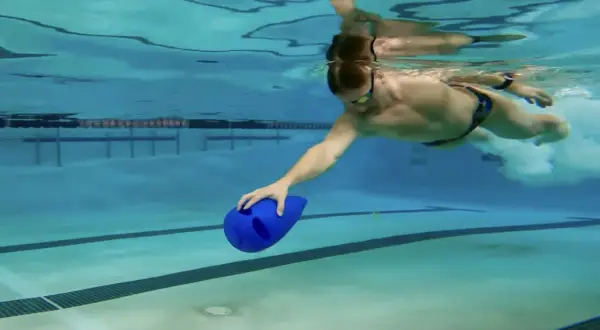 Man swimming underwater with a blue kickboard, practicing his kickboard swim technique.