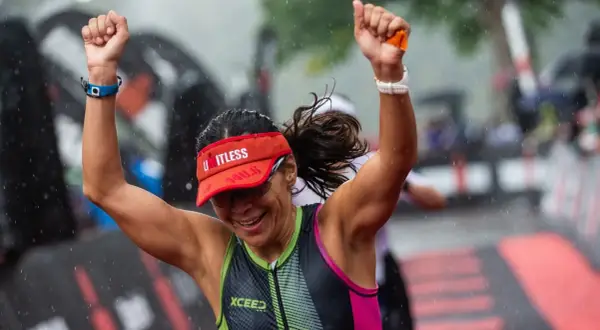 A triumphant athlete celebrates crossing the finish line of an Ironman length race in the rain.