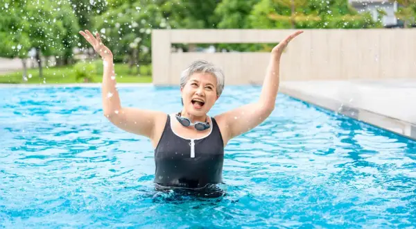 Joyful senior woman splashing water in a pool, enjoying her beginner swim workout.