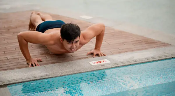 Man doing push-ups on a wooden deck next to a swimming pool.