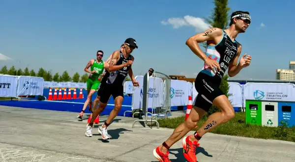 Triathletes push hard on the run course, a key part of their sprint tri training plan. Bright sun, blue skies, and a competitive spirit.