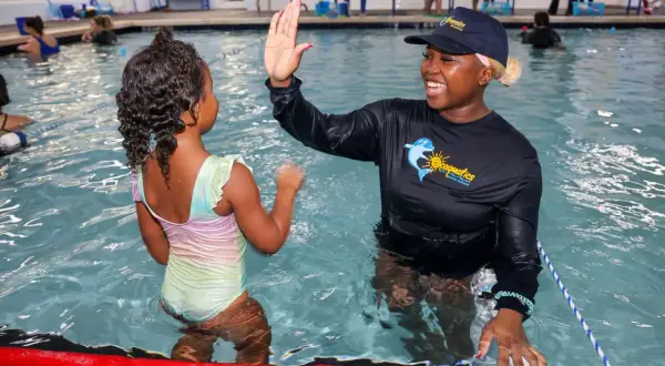 A swim instructor gives a young girl a high-five during swim stroke lessons.