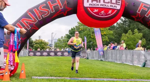 A woman crosses the finish line at a triathlon, smiling. This event is one of the best triathlons for participants to achieve their goals.
