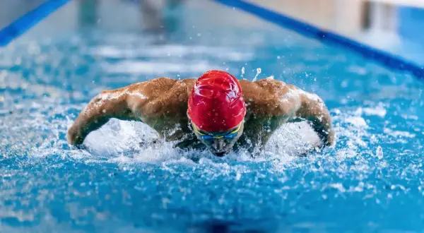 A swimmer in a red cap and goggles powers through the water, showcasing the strength and full-body engagement of breaststroke benefits.