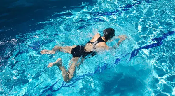 Swimmer in black suit performing breaststroke, showing the characteristic bent leg position of the breaststrokers knee.