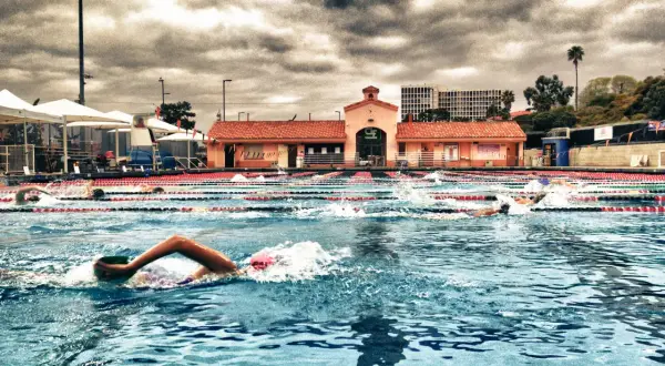 Swimmers race in an outdoor pool under a dramatic cloudy sky, enjoying a refreshing morning swim.