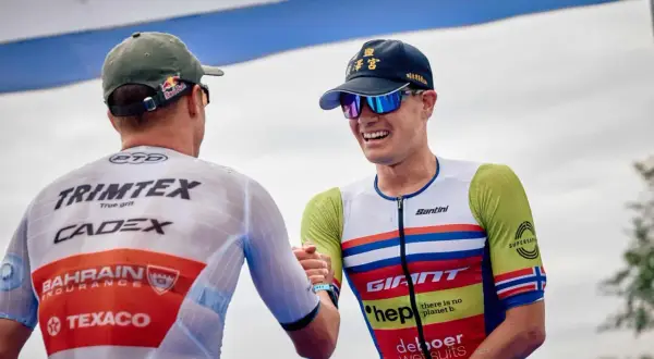 Gustav Iden, a triumphant triathlete, shares a handshake after a race, his smile wide and his racing suit vibrant.