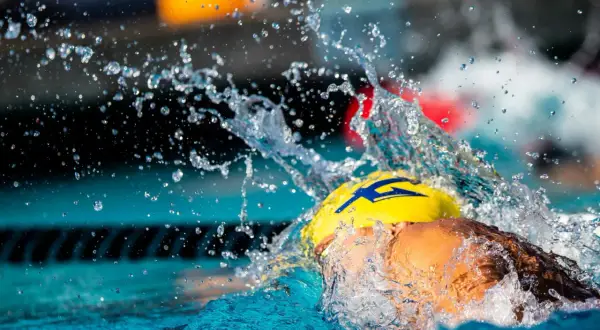 A swimmer in a yellow cap with a blue lightning bolt, mid-stroke, creating a dramatic splash. This captures the intense swolf meaning of speed and power.