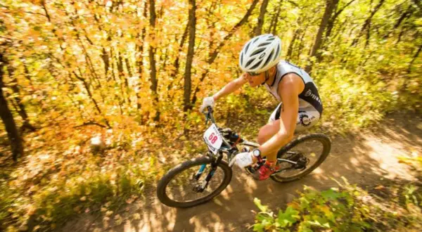 Athlete races through an autumn forest during an off road triathlon, navigating a dirt path with colorful foliage.
