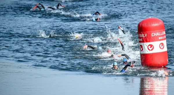 Athletes compete in a triathlon, their triathlon swim strokes creating splashes as they navigate the water around a red buoy.