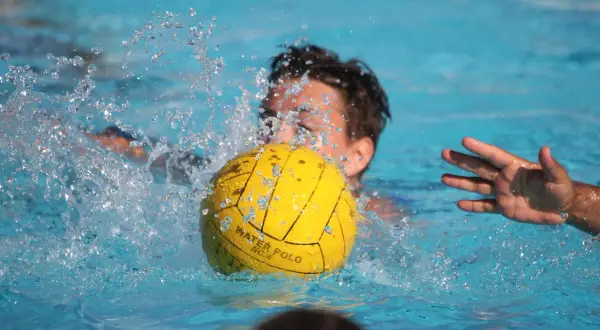 A young player in a water polo match splashes water as they go for the ball.