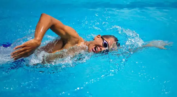 Swimmer with goggles in bright blue water, performing bilateral breathing during a freestyle stroke.