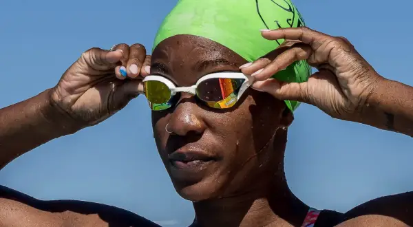 A swimmer adjusts her goggles, ready to dive in. She's proving you can swim with a burn, embracing the water.