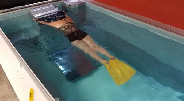 Woman with yellow fins practicing her leg kicking in a swim spa.