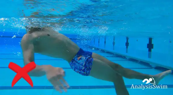 Underwater view of a swimmer demonstrating an incorrect backstroke arm movement. A red X marks the improper arm position.