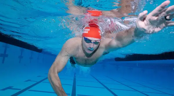 Underwater view of a swimmer performing a freestyle swim stroke, with arms extended and water splashing around.