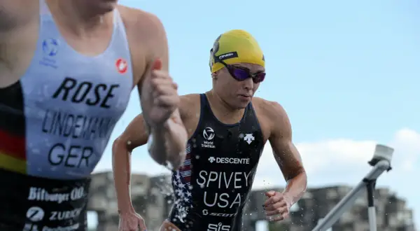 Taylor Spivey, a triathlete in a yellow cap and goggles, emerges from the water, her USA suit glistening.