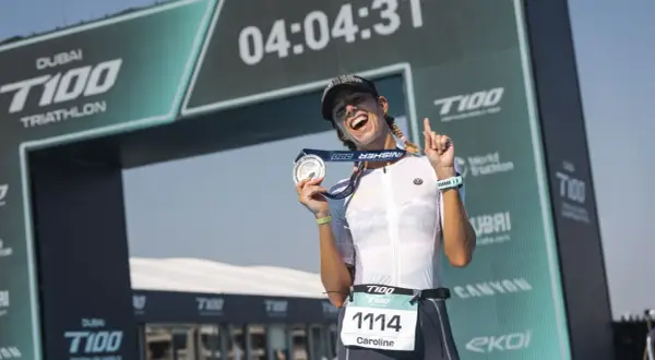 Caroline celebrates her finish at the Dubai T100 Triathlon, medal in hand, under the finish arch.