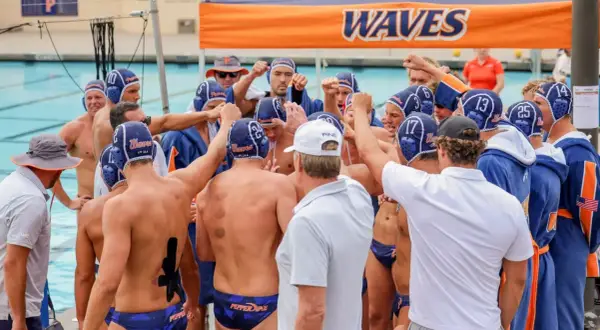 Waterpolo development: A team huddles, fists raised, showing unity and focus before a game.
