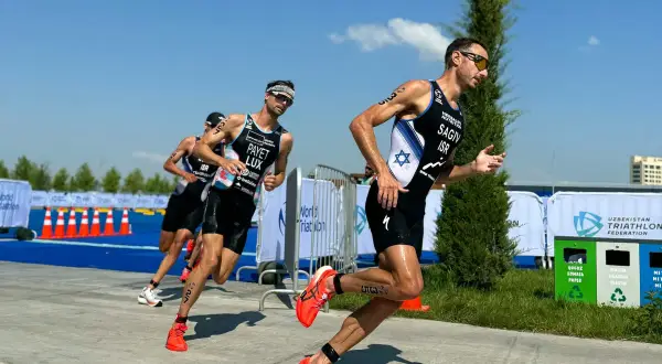 Athletes in racing gear push forward during a triathlon training run, focused and determined under a bright blue sky.
