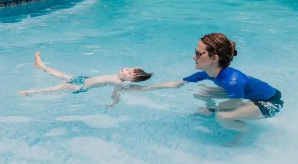 A child floats on their back in a pool during ISR swim lessons, with an instructor reaching out to support them.