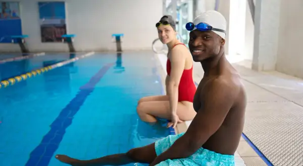 Smiling adults in swim gear at pool edge, ready for swim lessons for adults with fear of water.