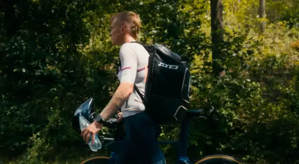 Athlete walks with bike and gear, preparing for the next stage in triathlon transition areas.