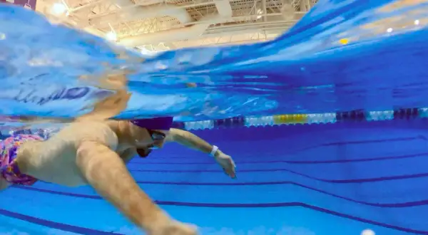 Underwater view of a swimmer in colorful trunks, demonstrating what is sculling with their arms to propel themselves through the blue pool water.