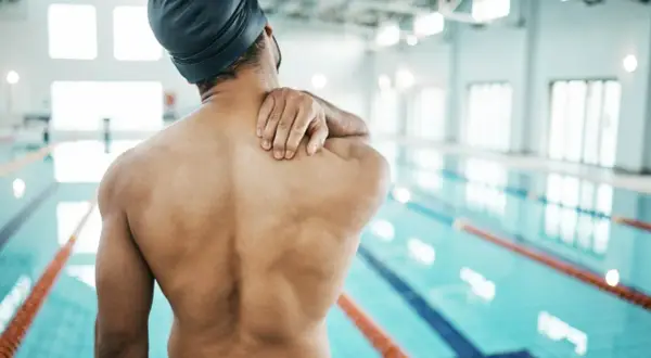 Swimmer holding shoulder in pain, questioning if you can swim with a torn rotator cuff.