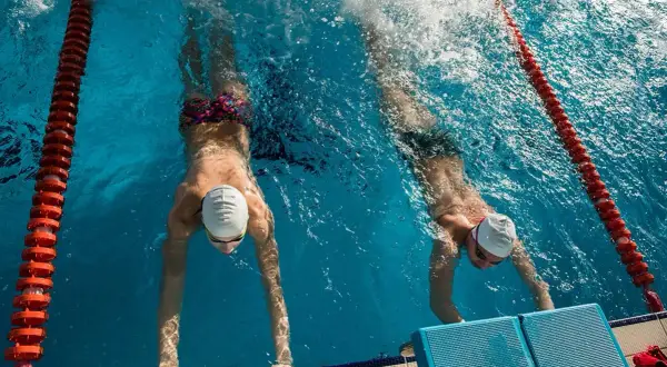 Two swimmers practice their flutter kicks, pushing off the wall in a race.
