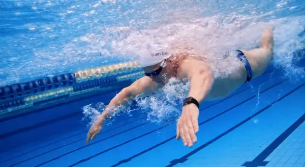 Swimmer executing a powerful butterfly stroke underwater, creating a splash as they propel through the blue pool lanes.