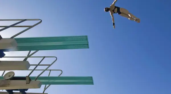 A diver in mid-air, performing a competitive dive against a clear blue sky.