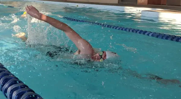 Swimmer pushing hard in a pool, arms extended, water splashing. This intense effort is part of a challenging vo2 max workout.