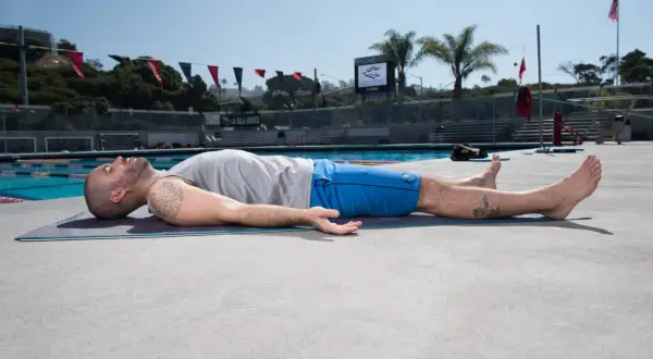 Man practicing yoga for swimmers, lying on a mat by the pool, enjoying a moment of relaxation and recovery.