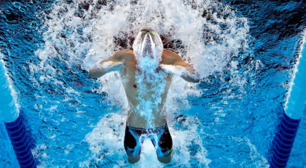 Swimmer powering through intense swim practice sets, creating a splash as they break the water's surface.