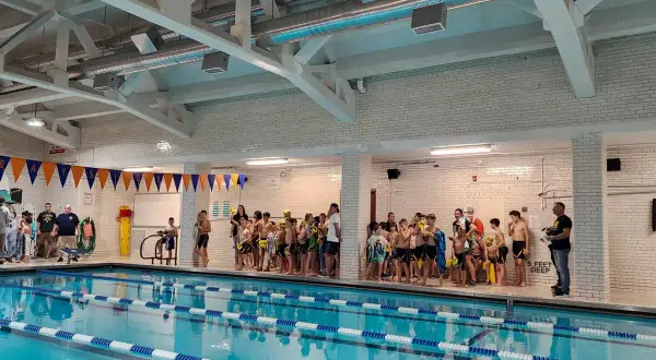 Children in swimsuits gather by the pool at Jim Montgomery Swim School, ready for lessons.