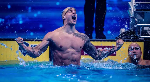 A triumphant swimmer, showcasing why swimmers have broad shoulders, celebrates in the water.