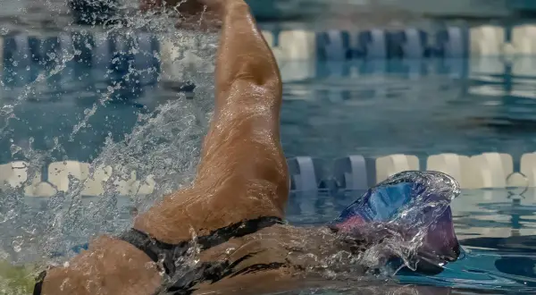 A swimmer's arm slices through the water, demonstrating the powerful stroke needed to swim laps. Water splashes around them as they focus on their technique.