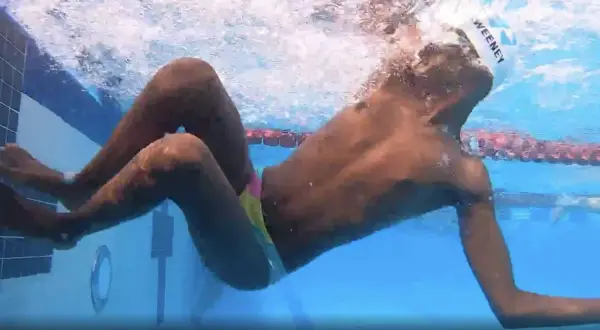 Underwater view of a swimmer performing a breast stroke, with arms extended forward and legs bent, showing the technique.