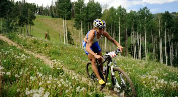 Athlete competes in a challenging mtb triathlon, navigating a grassy, dandelion-filled trail through a forest.