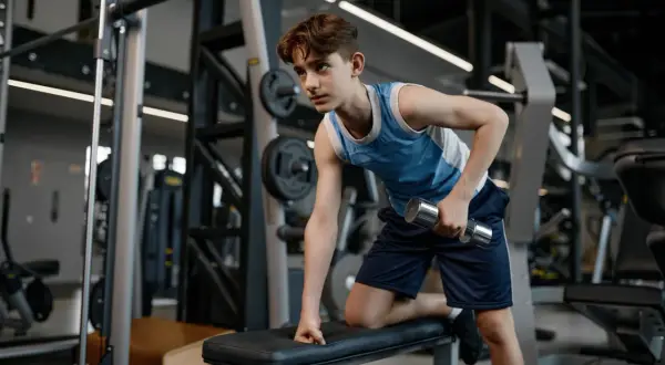 Young swimmer performing dumbbell rows as part of their cross training routine in a gym.